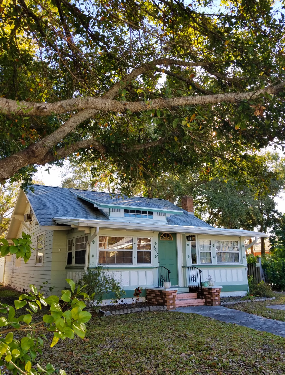 White bungalow with green trim under huge shade trees Gulfport Florida